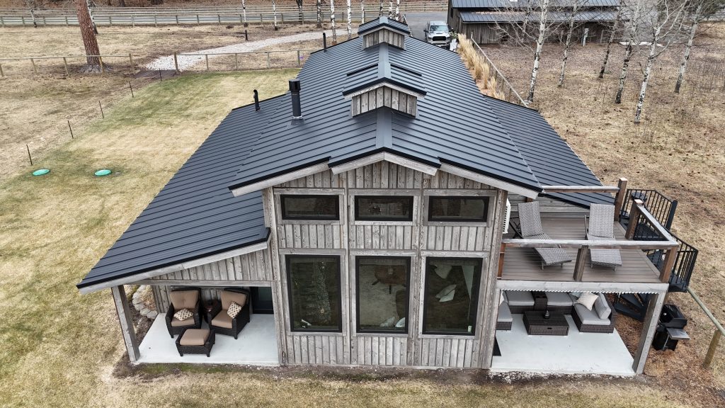 Barndominium with charcoal metal roof featuring large glass gable windows and covered outdoor living areas