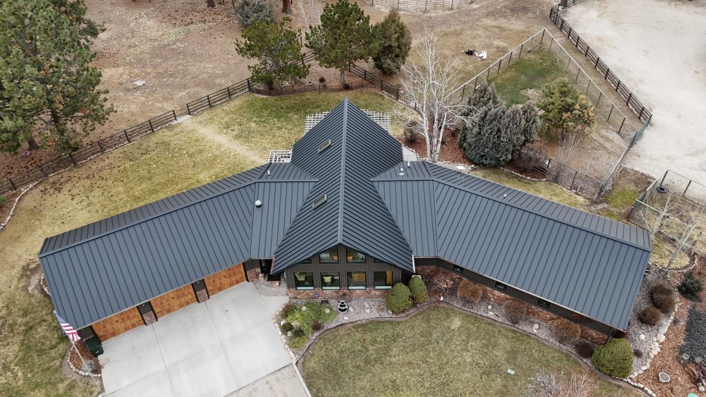 Wide aerial of large ranch home with charcoal standing seam metal roof and cedar garage doors on rural property