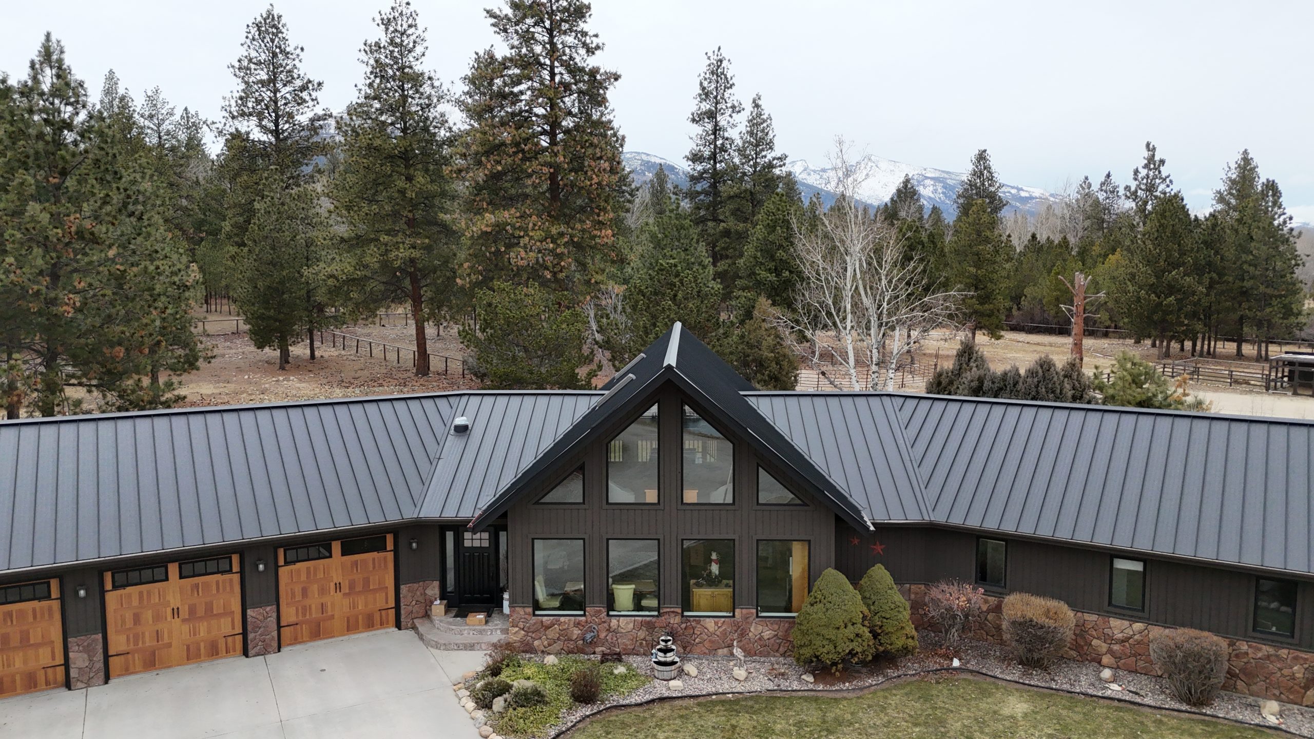 Front aerial view of ranch home with charcoal metal roof featuring large glass gable and mountain backdrop