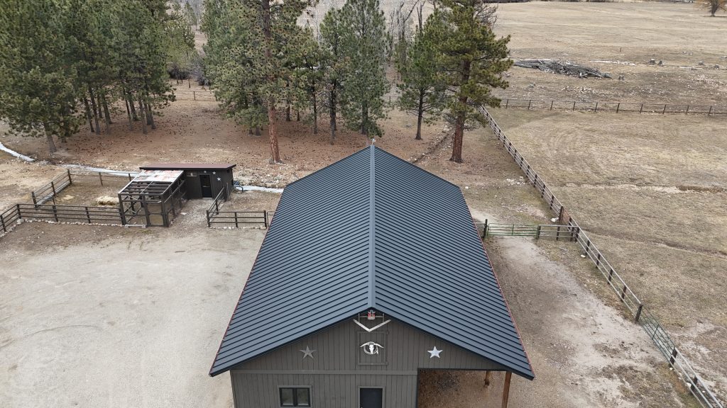 Aerial view of small ranch barn outbuilding with charcoal standing seam metal roof and decorative star accents