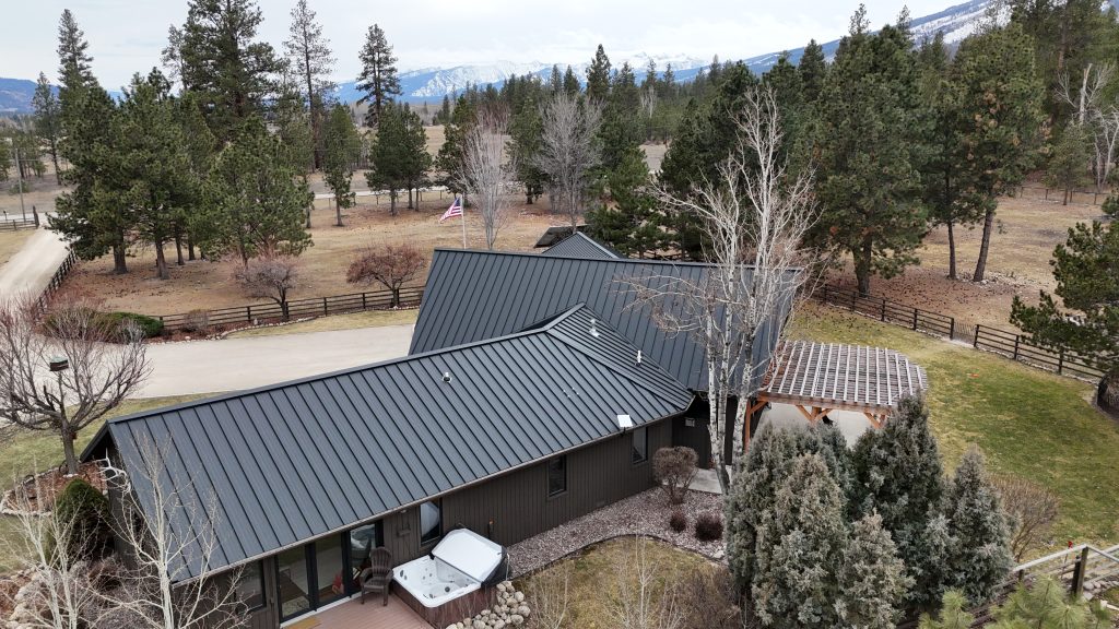 Ranch home with charcoal metal roof featuring timber pergola and hot tub with mountain backdrop