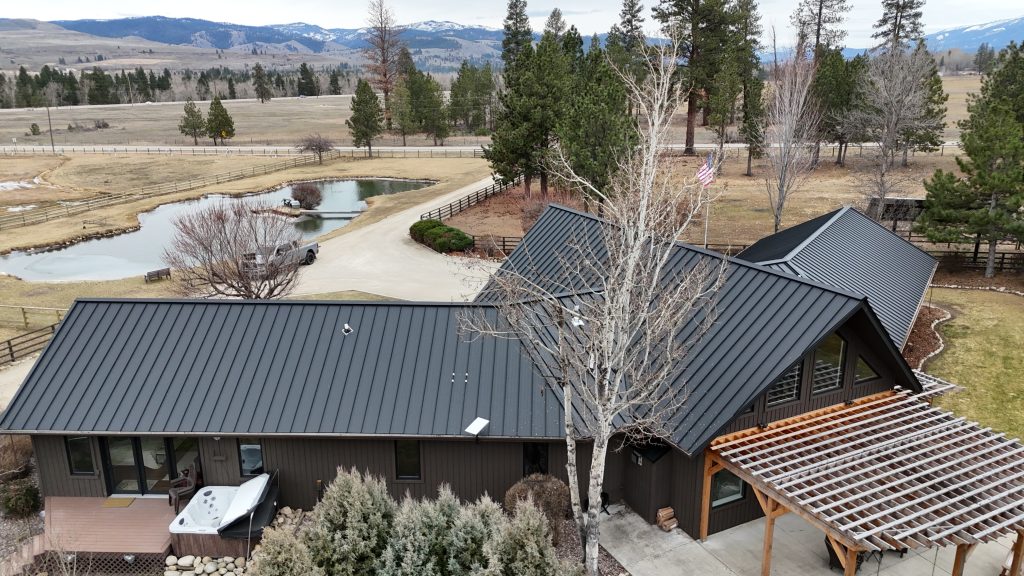 Aerial of ranch home with charcoal metal roof overlooking private pond and Montana mountain range