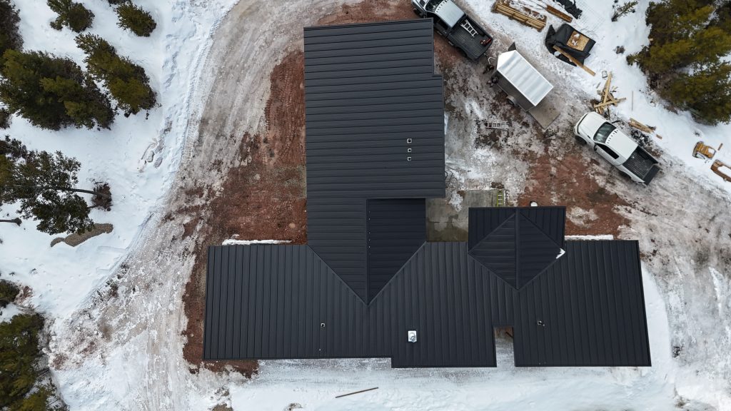 Drone overhead view of new construction home with black standing seam metal roof surrounded by winter snow