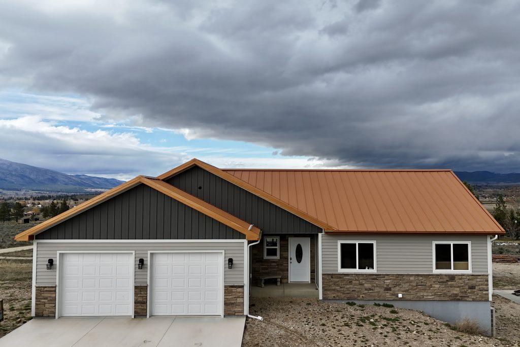 New ranch home with copper standing seam metal roof and stone veneer exterior with dramatic mountain and storm cloud backdrop