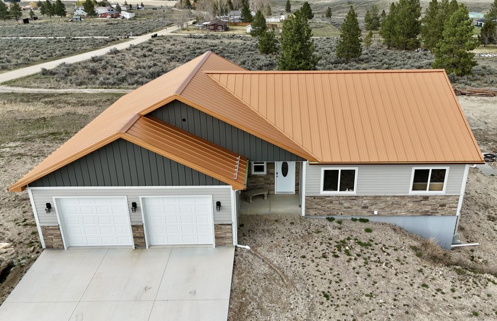 Front aerial view of ranch home with copper metal roof showing two-car garage and board and batten gable