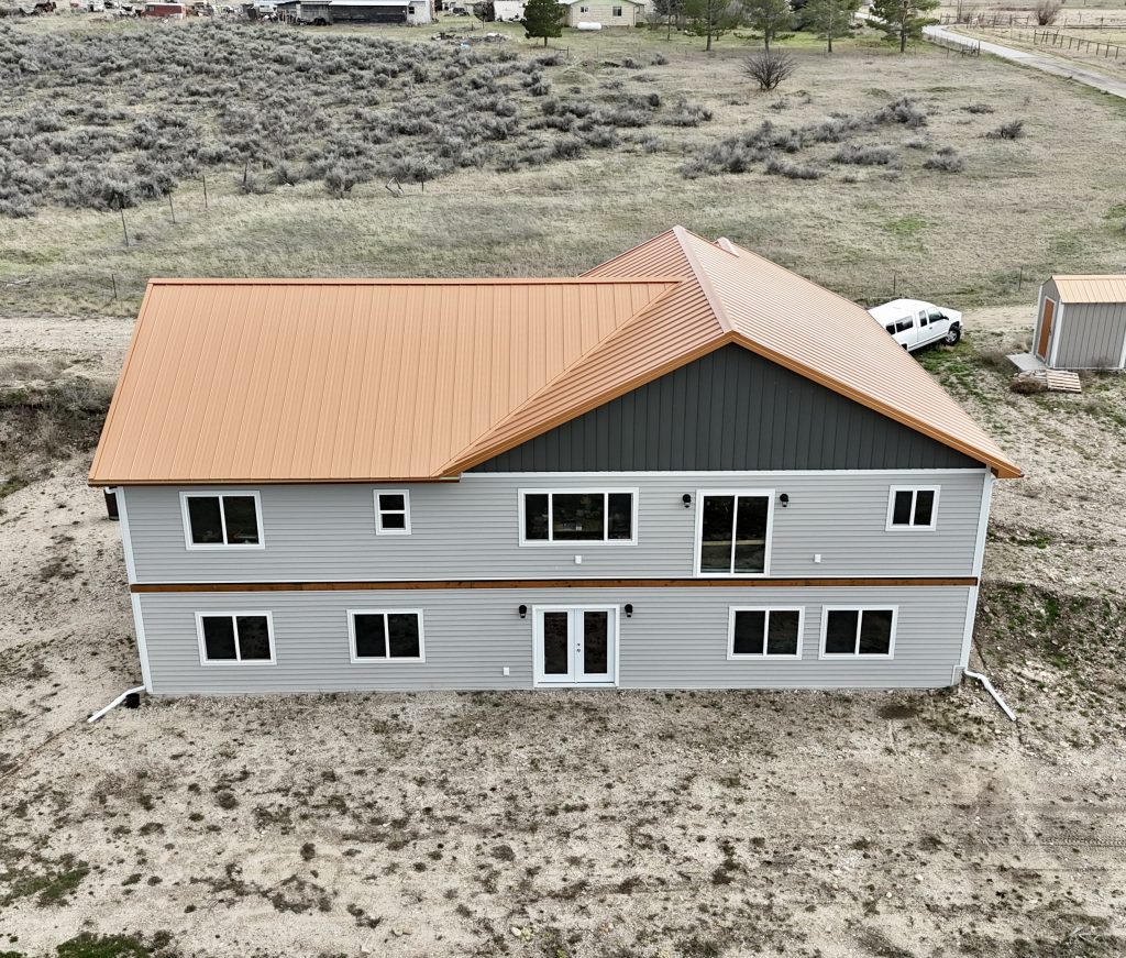 Rear aerial view of two-story ranch home with copper standing seam metal roof on rural Montana property