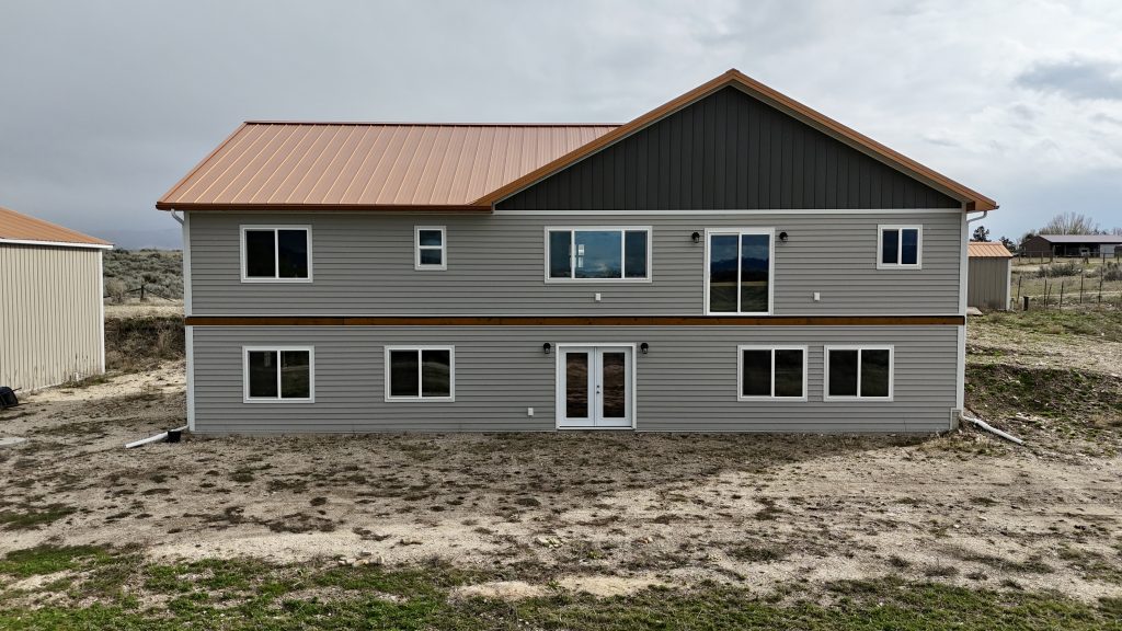 Rear ground-level view of two-story ranch home with copper metal roof showing full back facade and siding detail