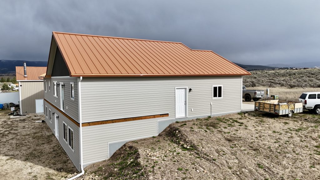 Side view of ranch home with copper metal roof against Montana mountain backdrop with storm clouds