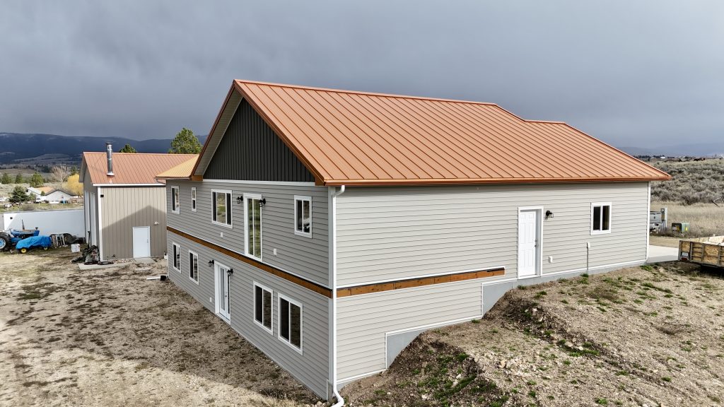Aerial side view of copper standing seam metal roof on ranch home with outbuilding in background