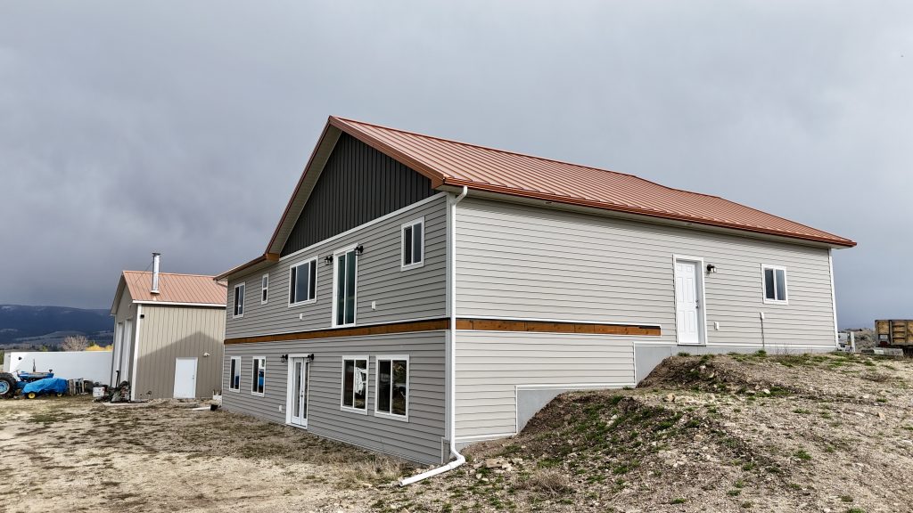 Low-angle aerial of ranch home featuring copper metal roof with board and batten gable and vinyl siding