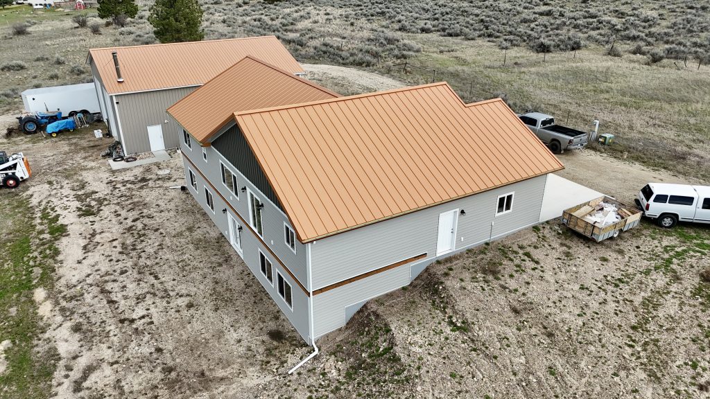 Aerial view of copper metal roof ranch home showing full property layout with outbuilding and sagebrush terrain