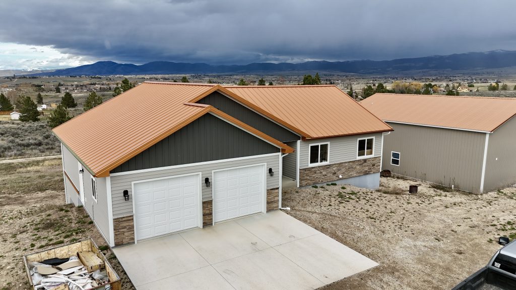Front view of ranch home with copper standing seam metal roof against dramatic Montana storm clouds and mountain valley