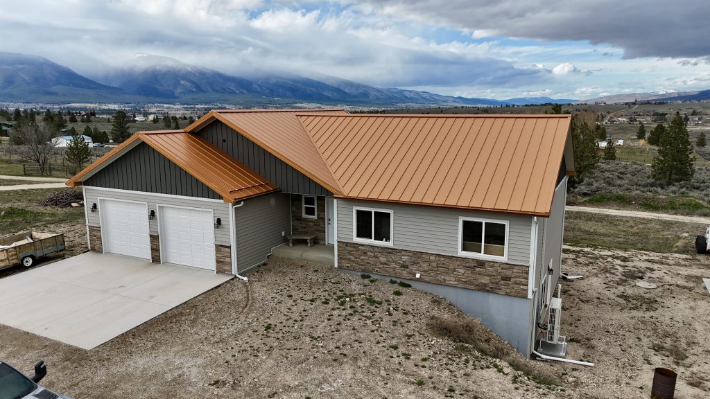 Front aerial of ranch home with copper metal roof overlooking expansive Montana valley with mountain range