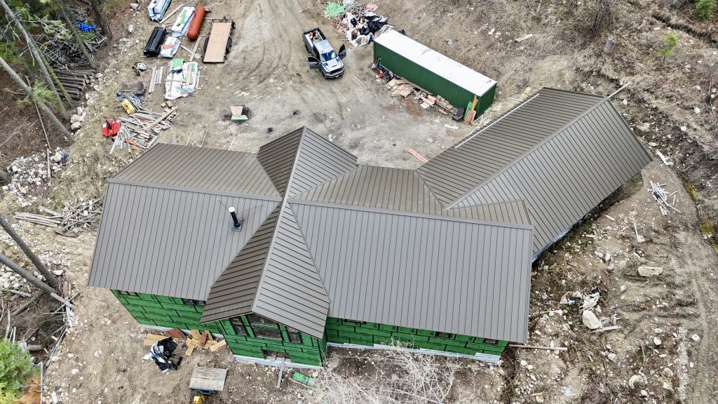 Overhead aerial of new construction home with bronze standing seam metal roof in forest setting with ZIP sheathing walls