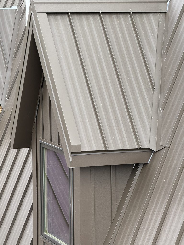 Close-up of bronze standing seam metal roof dormer showing precision panel installation and cap flashing
