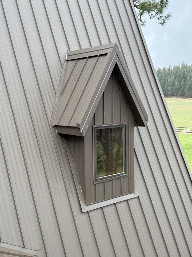 Detail shot of peaked metal dormer with standing seam panels over window on charcoal metal roof field