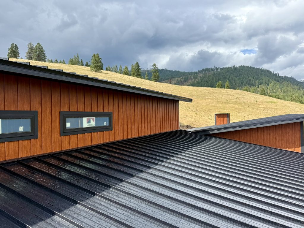 On-roof view of completed standing seam metal roof installation with Andersen windows and scenic valley and forested hillside in background