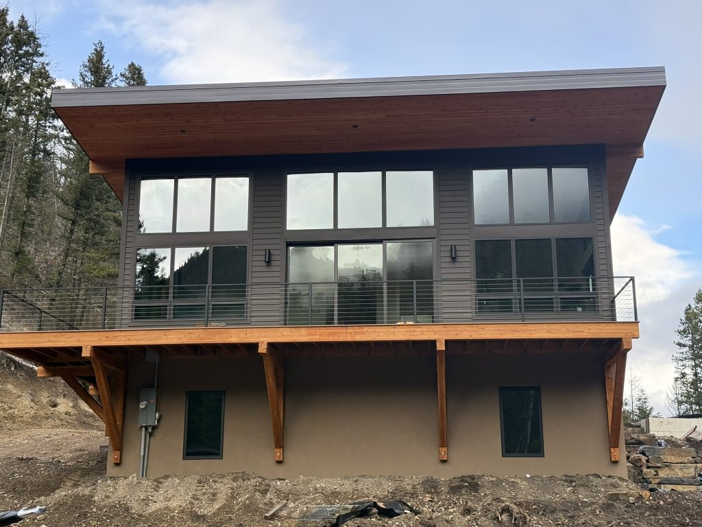 New construction modern home exterior with full-width panoramic windows wood soffit overhang timber knee braces cable railing balcony and stucco lower level