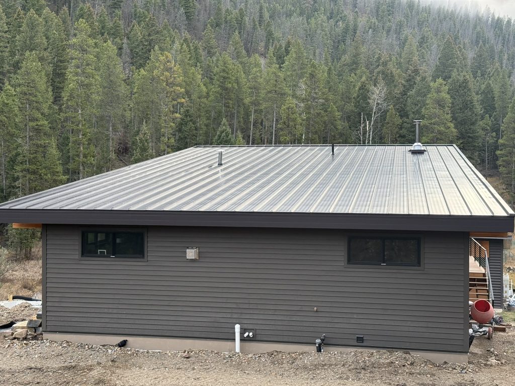 Rear exterior of modern new construction home featuring low-slope standing seam metal roof dark gray horizontal lap siding horizontal accent windows and mountain backdrop