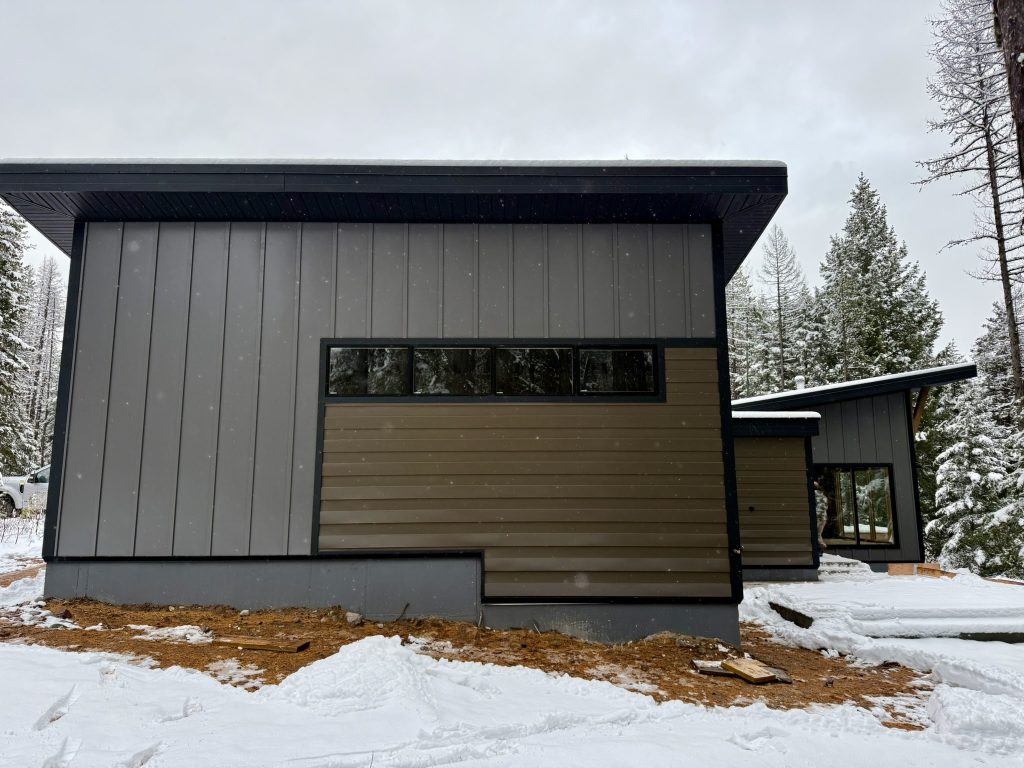 Rear view of modern home with gray vertical board and batten metal siding tan horizontal lap accent clerestory windows and dark metal fascia in winter