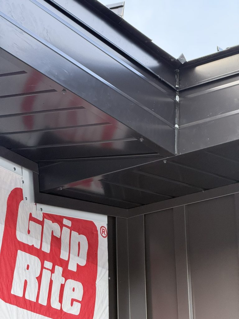 Close-up of black metal porch canopy with tongue-and-groove metal soffit panels and clean interior corner joint detail showing high-quality trim fabrication
