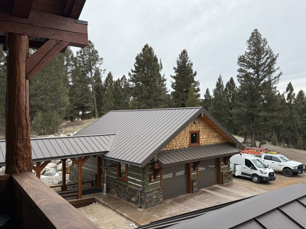 Elevated view of completed craftsman-style carriage house with brown standing seam metal roof cedar shake gable siding stone base and timber frame accents from upper deck