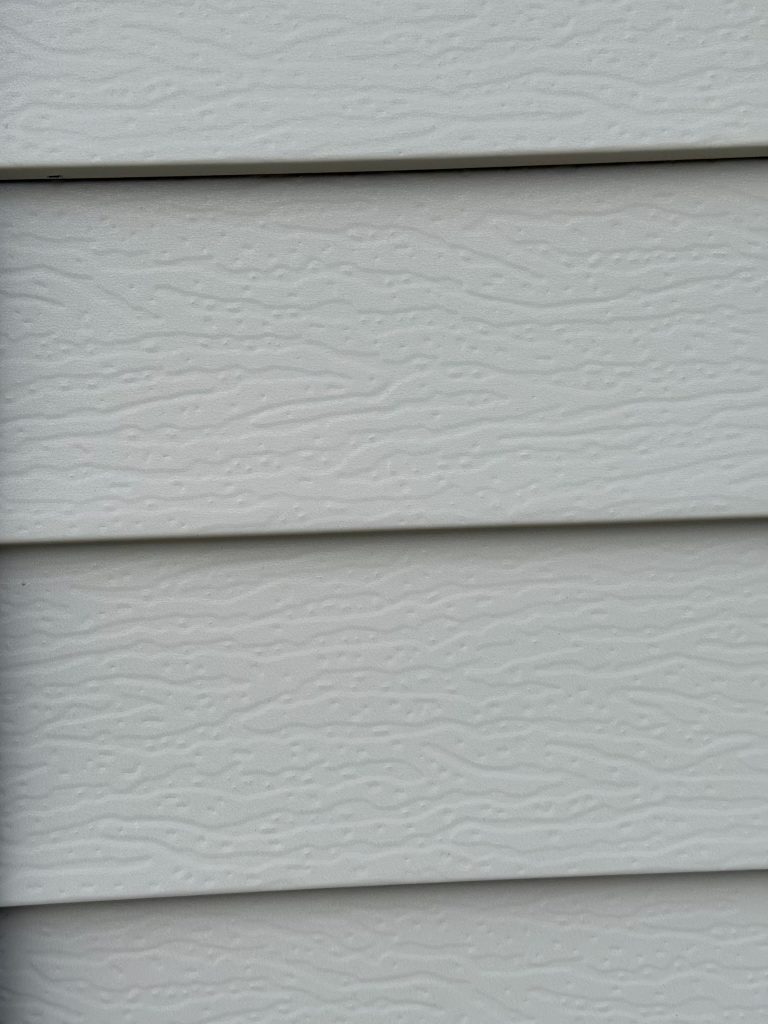 Macro close-up of light gray embossed lap siding panels showing wood-grain textured surface detail and panel overlap lines
