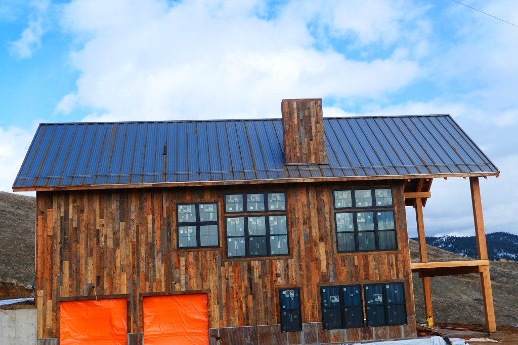 Side elevation of remote mountain cabin with silver galvalume standing seam roof reclaimed barn wood siding reclaimed wood chimney surround and large multi-pane black-framed windows