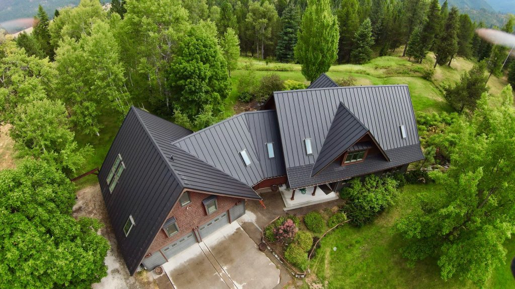 Drone view of multi-gabled home with black Crinkle standing seam metal roof in mountain forest setting